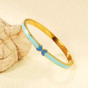 Elegant gold-tone bangle featuring symmetrical blue enamel heart motifs on a stone surface