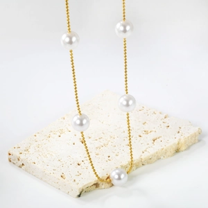 Elegant gold beaded necklace with five large white pearls on a natural stone base