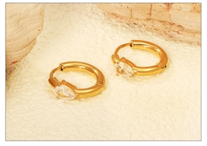 Dettaglio macro di orecchini huggie dorati con zirconi a goccia su sfondo di pietra bianca