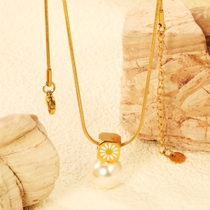 Collier chaîne serpent dorée avec perle blanche et pendentif marguerite sur fond de pierre