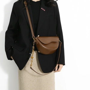 Brown leather saddle bag with gold chain and asymmetrical flap worn on a black suit