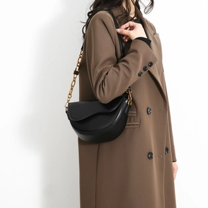 Classic black leather saddle bag with gold chain strap worn over a brown coat