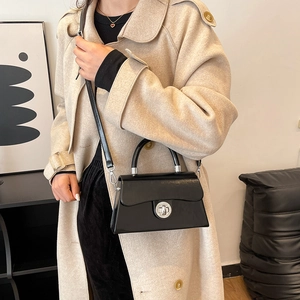 Sac boîte chic en cuir noir avec fermoir argenté porté sur un trench-coat beige