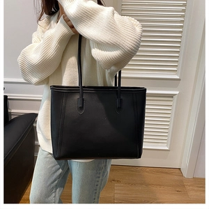Detailed view of black textured leather tote bag worn by a model in a casual setting