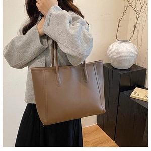 Detailed view of the large capacity brown tote bag worn on shoulder in a minimalist setting