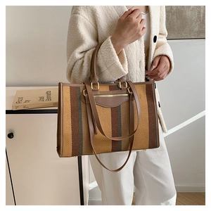 Macro detail of striped canvas tote bag with leather handles and premium gold hardware