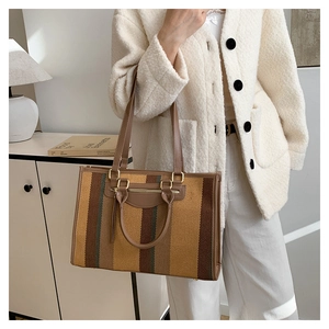 Detail view of colorful striped canvas tote bag with brown leather straps and metal hardware