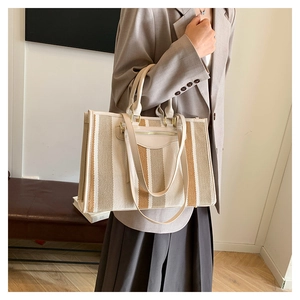 Detailed side view of a large striped canvas tote bag with leather trim in a cozy home setting