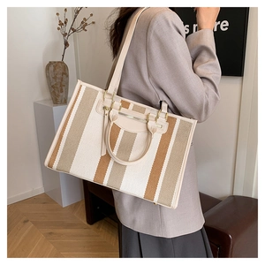 Detail of striped canvas tote bag showing textured vertical panels and metallic zippers