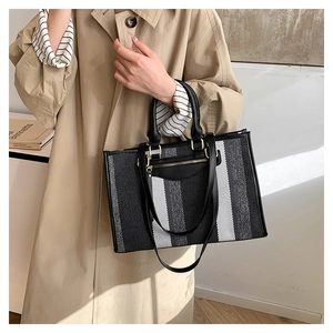 Model styling a large canvas tote bag with black, white, and grey vertical stripes