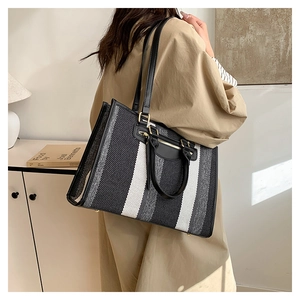 Detailed view of canvas tote bag with contrast stripes and leather handles shown by model
