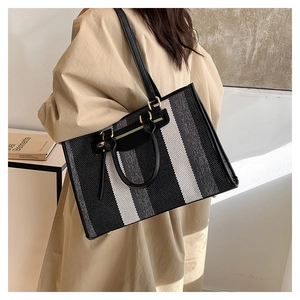 Detailed side view of a large striped woven tote bag with leather straps and gold buckles