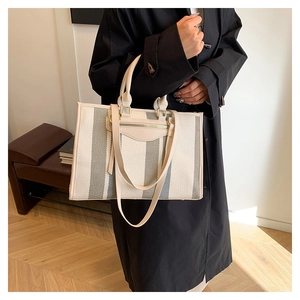 Model lifestyle view showing canvas striped tote bag with leather strap and handle detail