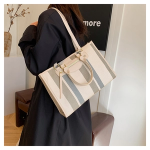 Model wearing a large striped canvas tote bag with dual handles and long shoulder strap