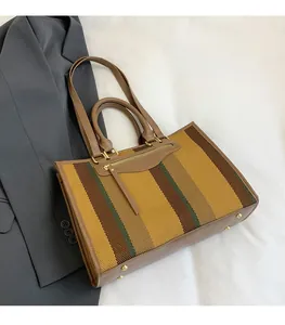 Detailed view of striped canvas tote bag with brown leather handles on grey background