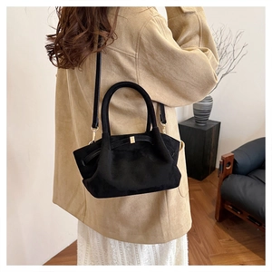 Détail du sac cabas en daim noir avec boucle dorée porté par un mannequin à la maison