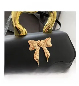 Detail of black leather handbag featuring a large gold heart-shaped handle and metal bow