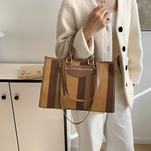 Large striped canvas tote bag with leather handles and adjustable shoulder strap shown by model