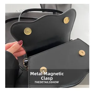 Detail of the golden circular magnetic snap closure on a black saddle-shaped handbag