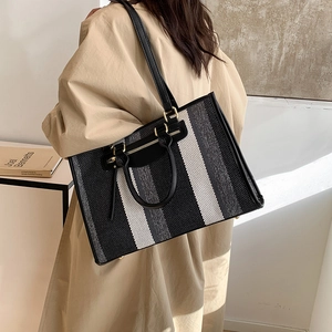Large striped canvas tote bag with black leather handles shown on a model's shoulder