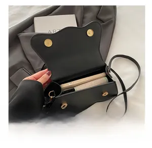 Detail view of the black small square crossbody bag with wavy flap and gold buttons