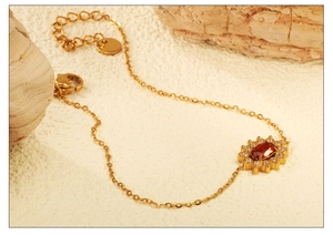 Detail of sunflower zircon bracelet with oval red gemstone and golden lobster clasp finish