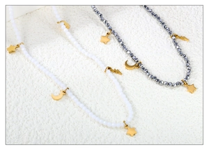 Détail de colliers de perles avec pendentifs étoile et lune dorés sur texture blanche