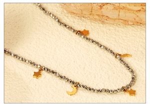 Détail du collier de perles avec pendentifs étoile et lune dorés sur fond texturé pierre