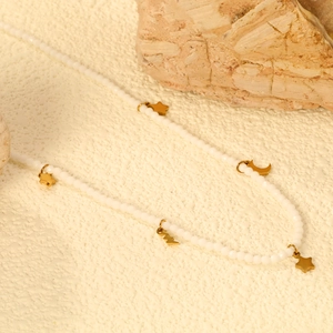 Collier en perles blanches avec pendentifs étoile et lune dorés sur fond texturé
