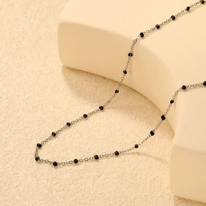 Détail d'un collier minimaliste avec perles noires sur un support géométrique moderne