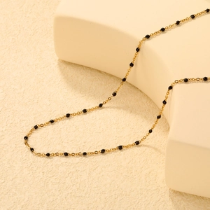 Collier en chaîne dorée minimaliste avec petites perles noires sur support géométrique