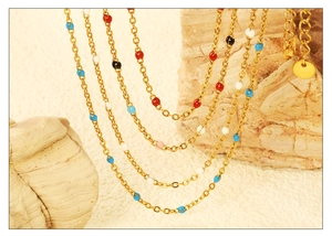 Detail of gold chain necklace featuring vibrant colorful enamel beads on a textured stone