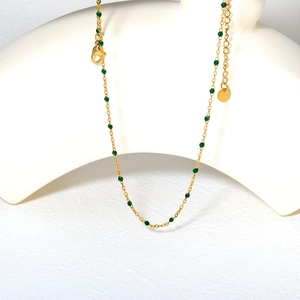 Detail view of a gold-plated stainless steel necklace with green enamel beads and clasp