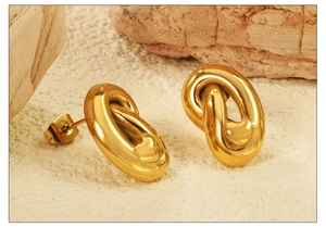 Detail of gold metal oval earrings with small heart accents on natural rock texture