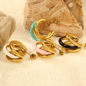 Three-layer C-shaped gold hoop earrings with colorful enamel details on stone background