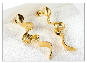 Detail view of wave-shaped gold-plated metal earrings with modern twisted artistic design