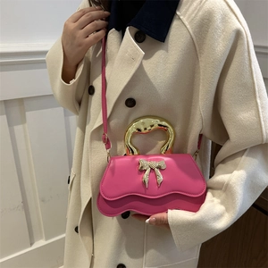 Pink PU leather crossbody bag with golden metal handle and bow detail on beige coat