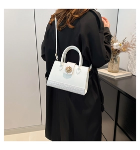 Detalle de bolso blanco con diseño de cocodrilo y cierre floral dorado sobre abrigo