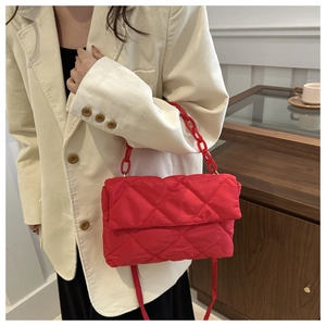 Detail of red quilted puffer crossbody bag with bold plastic chain handle and strap