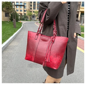 Detail of burgundy tote bag featuring woven handles and stylish leather tassel charm