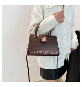 Gros plan d'un sac à main marron avec texture croco et boucle fleur dorée sur modèle