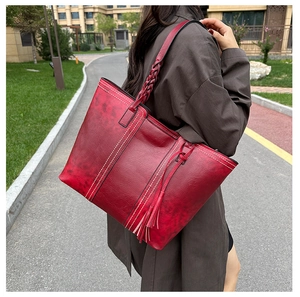 Detail of dark red vintage tote bag featuring woven handle and fringe tassel accessory