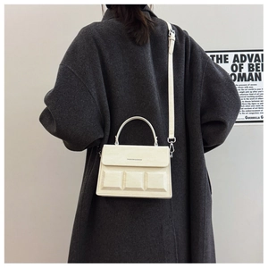 Detail of cream box bag with geometric chocolate patterns worn over a grey coat