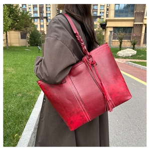 Detail of red leather tote bag with white contrast stitching and tassel charm in sunlight
