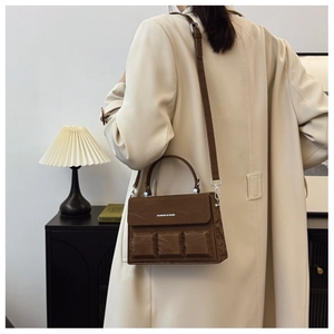Detail of a dark brown box bag with chocolate square texture and cross-body strap