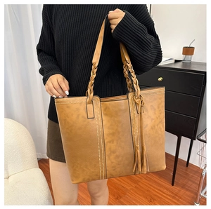 Close-up of caramel brown tote bag featuring woven handle and fringe tassel detail