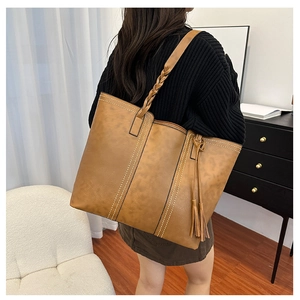 Detail of caramel brown tote bag featuring woven straps and elegant side fringe tassels