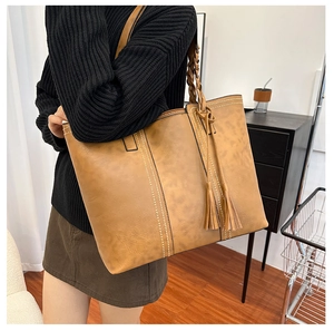 Detail of caramel faux leather tote bag with contrast stitching and tassels on a model