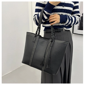 Detail of black tote bag with woven handles, white stitching, and leather tassel charm