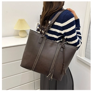 Detail view of large brown tote bag with contrast stitching and woven shoulder strap